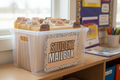 Plastic crate on classroom shelf with neutral-toned arch tab labels and Student Mailbox sign